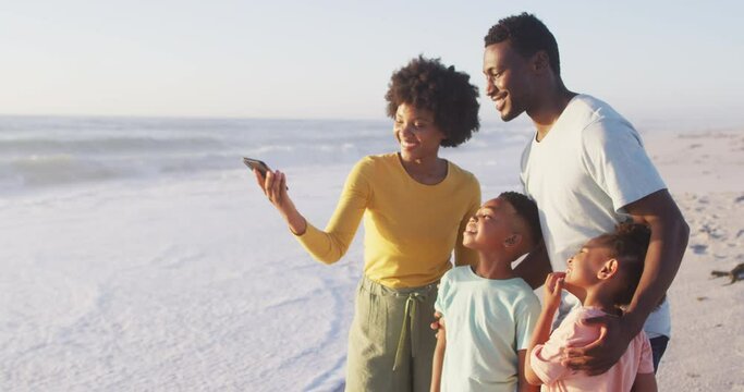 Smiling african american family taking selfie and embracing on sunny beach
