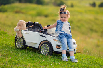 girl sits on the hood of a children's car that stands on the lawn