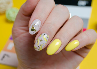 The hands of a young woman with yellow gel polish and a design with bananas. Manicure ideas for spring and summer