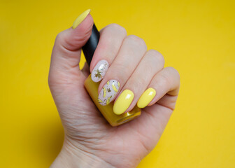 The hands of a young woman with yellow gel polish and a design with bananas. Manicure ideas for spring and summer