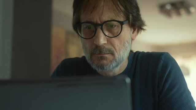 a serious mid adult man working at laptop. dolly shot