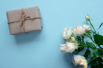 Obraz na płótnie Canvas A gift in craft paper next to a spray rose on a blue background. Holiday postcard. Holiday gift. Spring background. Pastel background.