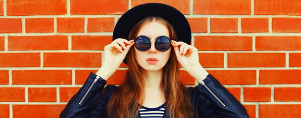 Portrait close up of stylish young woman model wearing black rock style on brick wall background