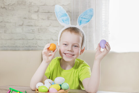 Easter kids. Happy boy in rabbit ears on his head plays with colored eggs at home. Preparing for Easters the Big Egg Hunt. Easter Bunny. Easter eggs.