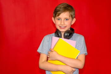 smiling schoolboy with headphones holds notebooks in his hands. owl to school happy child. the end of the school year. red background