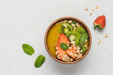 Mango smoothie wooden bowl with granola, kiwi and strawberries. Healthy vegan diet food concept