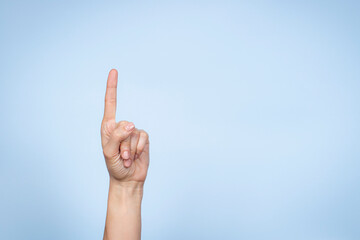 Hand gesture. Female hand shows number one. Woman pointing up with index finger on light blue background