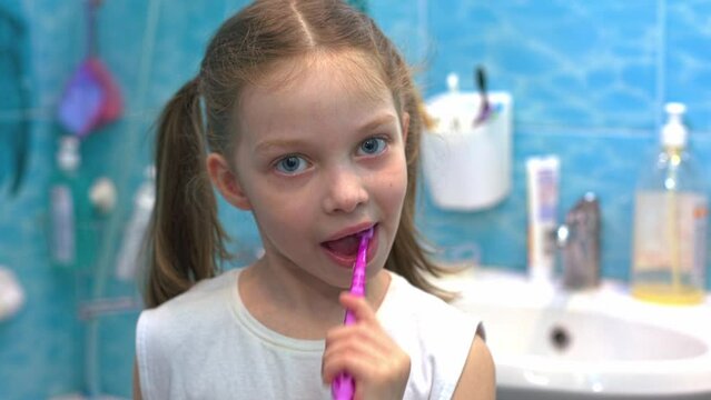 a little six-year-old girl brushes her teeth in the bathroom in front of a mirror, oral hygiene