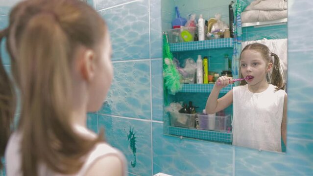 a little six-year-old girl brushes her teeth in the bathroom in front of a mirror, oral hygiene