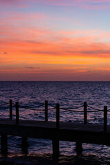 Fototapeta premium Rope bridge silhouette at sunset. Beautiful seascape, bright orange sky and sea