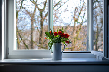 tulips in a vase in front of a window with a tree in the background