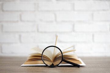 open book with magnifying glass on the table, copy space over white brick wall background