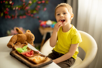 Cute little preschool child, boy, eating dried fruits at home, strawberries, melon, pineapple - obrazy, fototapety, plakaty
