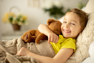 Cute little preschool boy with his pet dog, playing together in bed