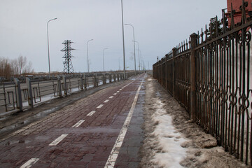 Fototapeta premium Spring roadside and sidewalk. Sidewalk along the highway and melting snowdrifts in spring