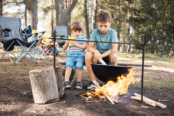 Children sitting around a campfire in forest in summer. Family picnic outdoors. Camping life....