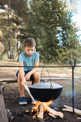 Teenage boy sitting around a campfire in forest in summer. Family picnic outdoors. Camping life....