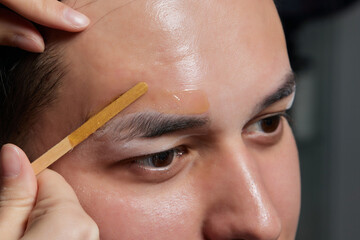 Professional barber doing threading procedure and correcting shape of eyebrows to young male client...