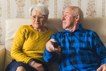 Portrait of an elderly couple watching television while sitting on the sofa - man is holding the remote control. High quality photo