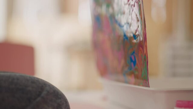 Artist takes out sheet covered with abstract patterns in Ebru style off tray at small table in studio extreme closeup slow motion. Oriental marbling technique
