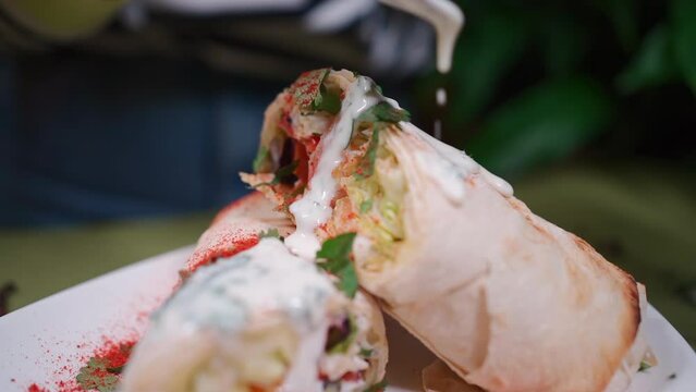closeup of hand with spoon add souce on shawarma with meat, salad and vegetable