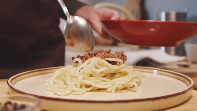 Close up shot of unrecognizable woman adding bolognese sauce to freshly cooked homemade spaghetti on plate