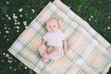 Cute happy baby lying on blanket on green grass at summer outdoors. 3 months old barefoot baby on...