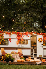 camping autumn. photo studio. Trailer on the background of the forest. Flowers in pots.Wooden table and chairs near the trailer. Autumn scenery