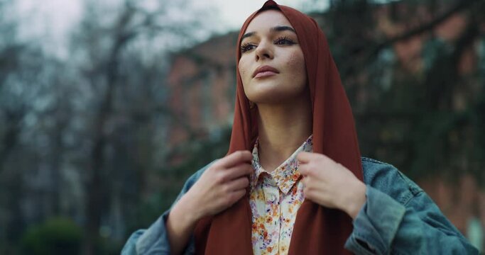 Cinematic shot of young happy Arabian muslim woman is adjusting her hijab and smiling  in camera outdoors.