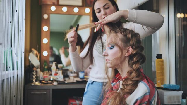 The girl makeup artist makes a braid for the model.