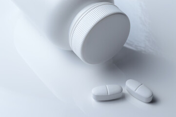 white plastic medicine jar and two white pills. light background