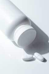 white plastic medicine jar and two white pills. light background