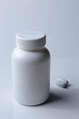 white plastic medicine jar and two white pills. light background