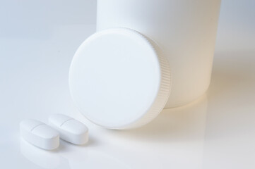 white plastic medicine jar and two white pills. light background