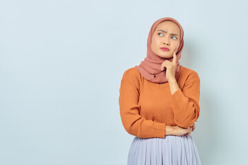 Fototapeta premium Portrait of beautiful young Asian Muslim woman in brown sweater looking serious thinking about question and looking at copy space isolated on white background. Muslim lifestyle concept