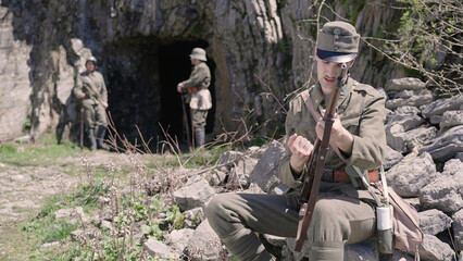 Austro-Hungarian soldier check the rifle while sitting on rock by military cavern