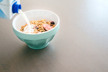 Milk pouring into bowl of fresh muesli,  side view with copy space,   isolated on wooden background. Healthy breakfast concept.