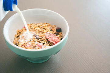 Milk pouring into bowl of fresh muesli,  side view with copy space,   isolated on wooden background. Healthy breakfast concept.