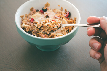 Young man's hand with muesli bowl, using spoon for eating cereals with fruits and milk as a breakfast concept. Healthy snack in the morning.