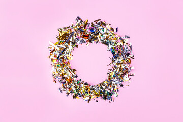 On a pink background, a circle of shiny multi-colored confetti. Festive background with place to insert text. Copy space