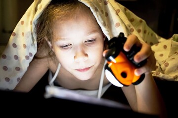Cute little girl hides under a blanket and reads a fairy tale about a magical space world