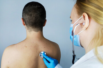 Young man at the doctor's office. The doctor, a young woman, carefully listens to his heart, lungs with a phonendoscope. Family doctor.