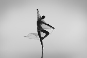 Black and white portrait of graceful ballerina dancing with fabric, cloth isolated on grey studio background. Grace, art, beauty concept. Weightless, flexible.