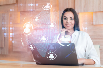 Attractive businesswoman in white shirt at workplace working with laptop to hire new employees for international business consulting. HR, social media hologram icons over office background