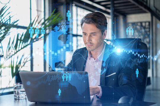 Handsome businessman in suit at workplace working with laptop to hire new employees for international business consulting. HR, social media hologram icons over office background