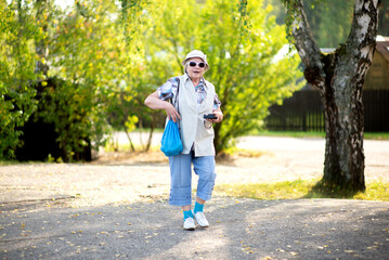 A smiling elderly woman with a shoulder bag and a camera goes on a hike