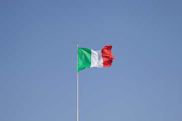 Italian flag waving on a pole against a clear blue sky
