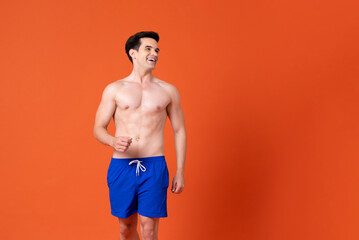Handsome shirtless Caucasian man wearing summer short pants smiling and looking aside in colorful...