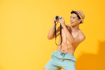 Shirtless young handsome Asian tourist man wearing summer short pants taking picture with camera in...