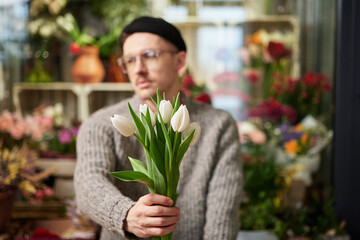 Mother's Day, dating, love, romantic or International Women's Day concept. Bearded florist male in sweater holding out at camera beautiful bouquet of spring white tulip bouquet. High quality photo